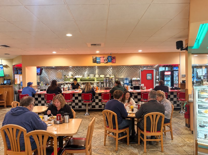 A full counter of guests on red chrome stools at the checkerboard bar