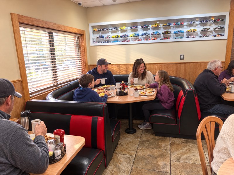 A family eating breakfast in the corner booth under the toy-car wall